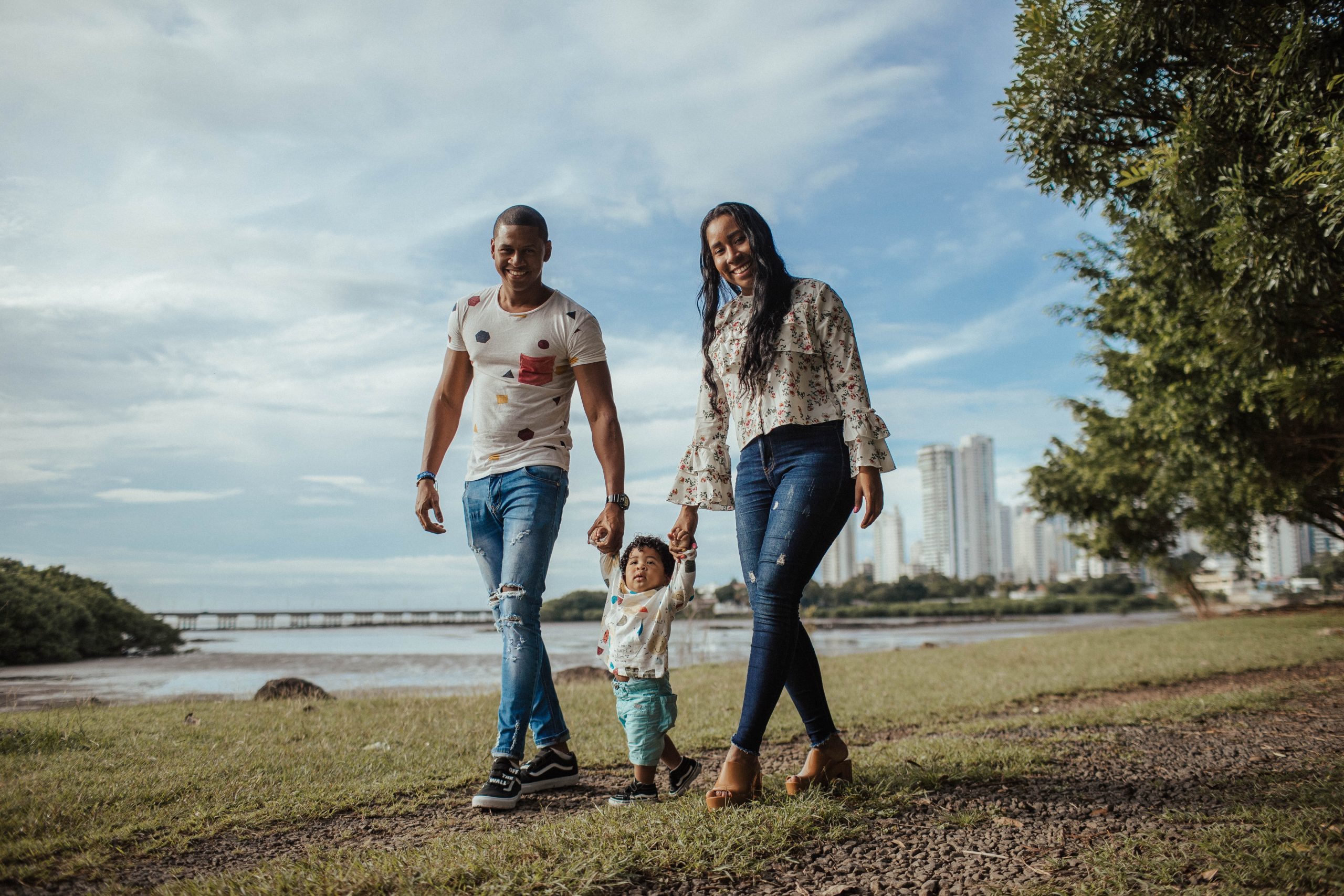 Photo of a man and woman parent couple walking through a park, each holding the hand of a toddler walking between them, symbolic of children and family services providerd by Volunteers of America Southwest.