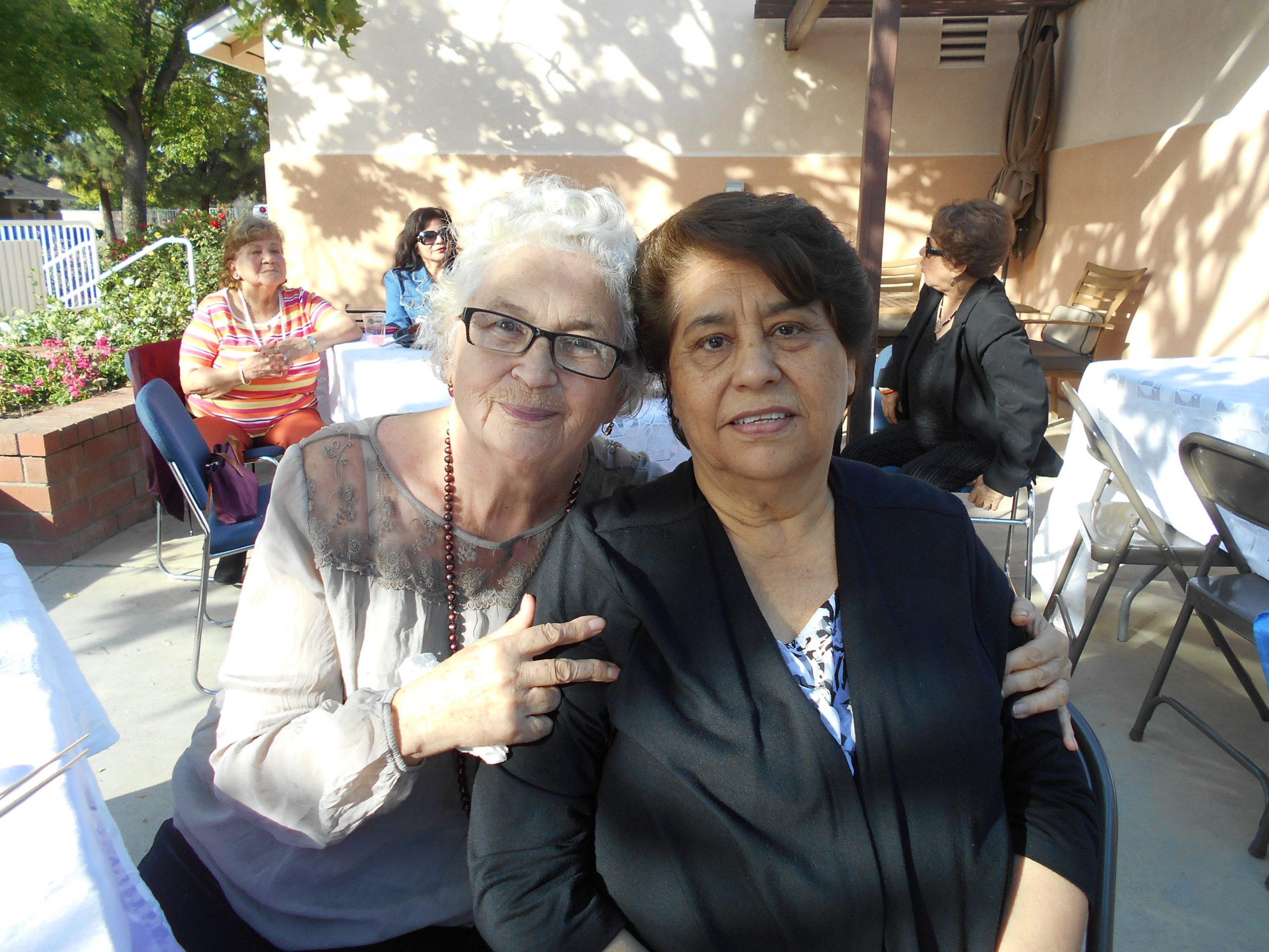 Two senior women, one with white hair and one with brown hair, sitting and posing for a picture at Cambridge Gardens senior housing community.