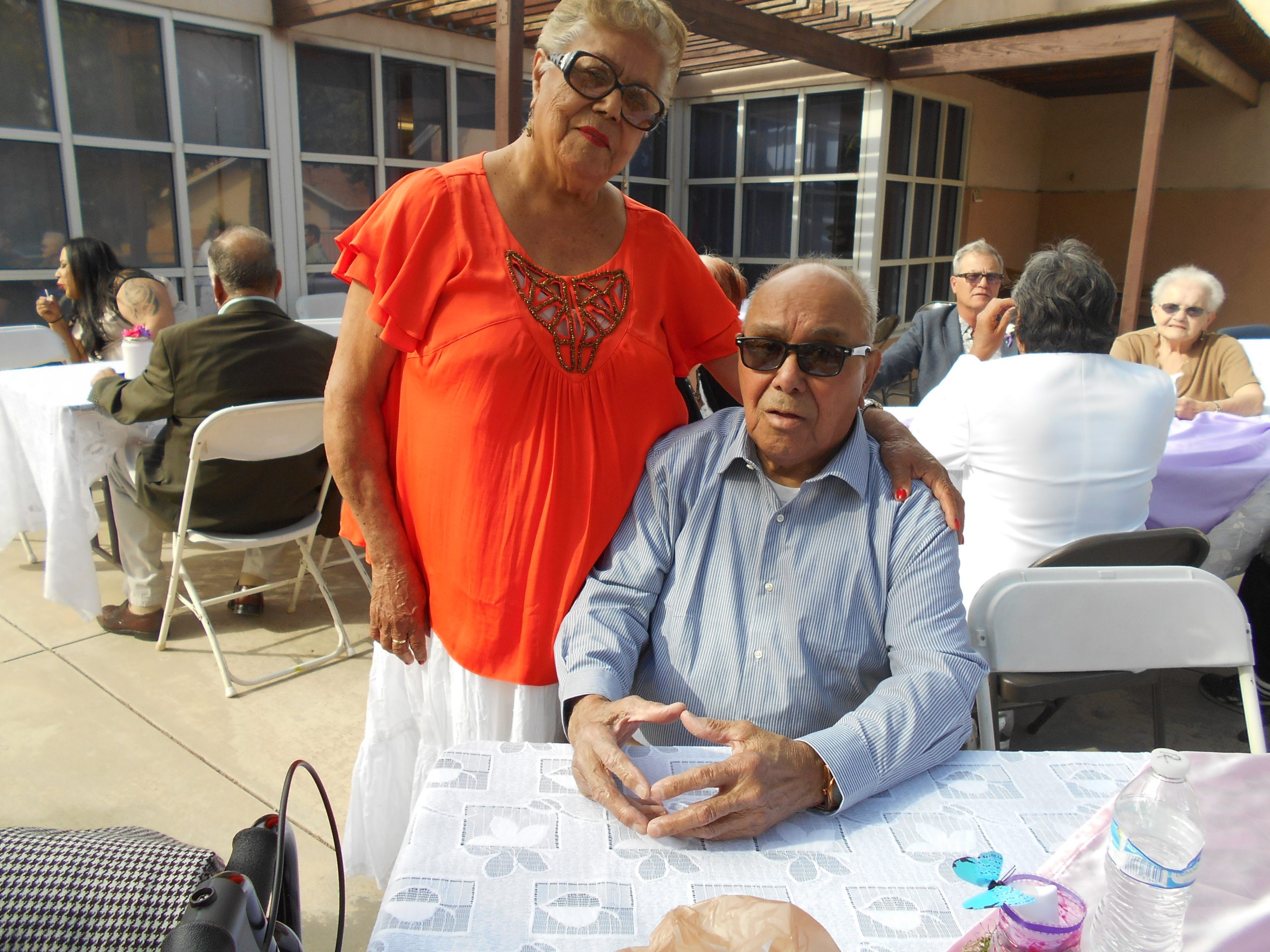 A man in a blue shirt and a woman in an orange shirt posing for a picture from behind a table at Cambridge Gardens senior housing community.