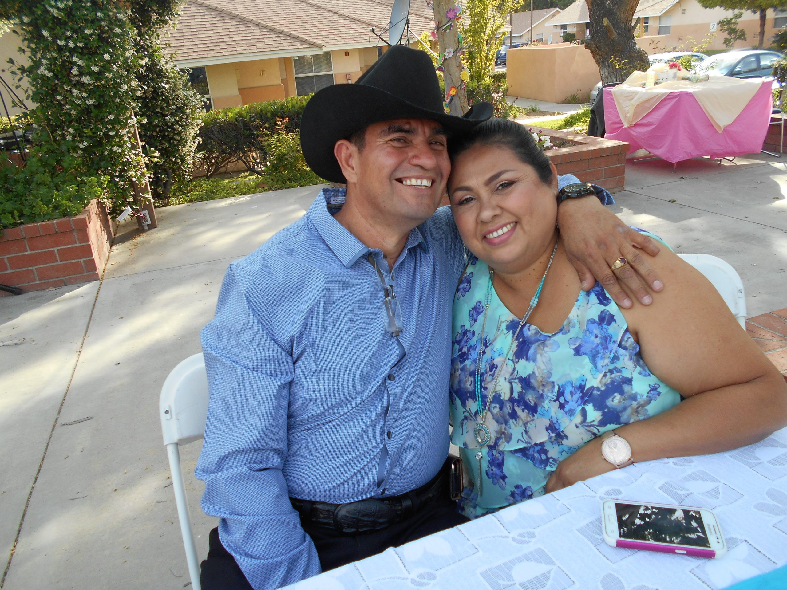 Photo of a latinx man and woman, the woman in a flowered top and the man in a blue shirt and cowboy hat, at Cambridge Gardens senior housing community.
