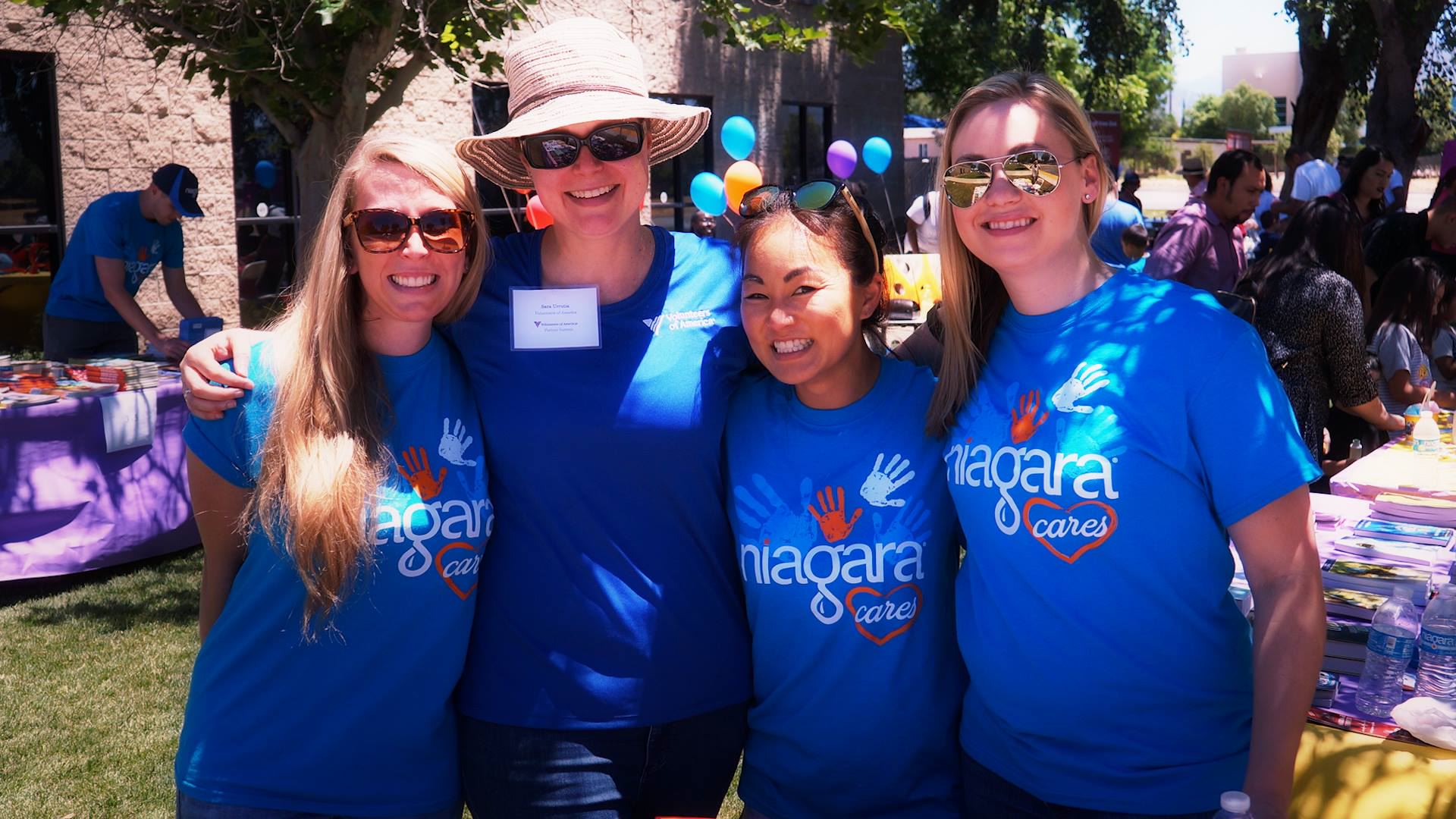 Photo of four women in blue t-shirts smiling and posing for a picture while performing nonprofit volunteer work.