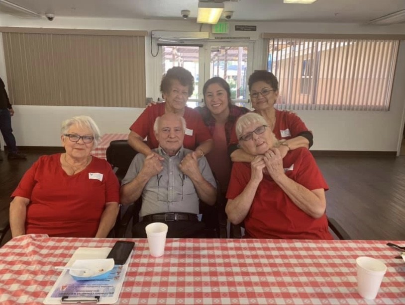 A group of seniors sitting inside at a table covered in the classic red and white checkered picnic pattern at Cambridge Gardens senior housing community.