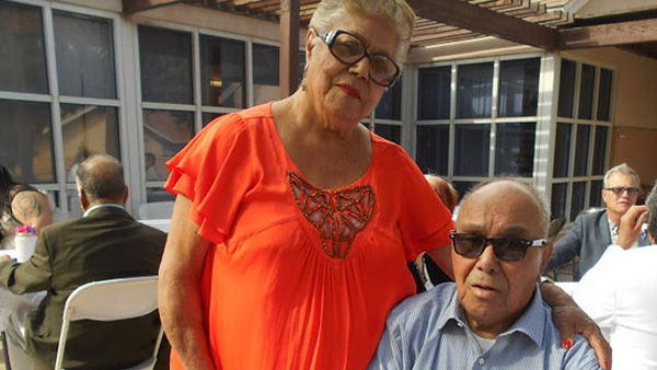 Two African American seniors, a woman in an orange shirt and a man in a blue shirt, both wearing glasses pose for a picture at Cambridge Gardens senior housing community, symbolizing the positive affect of supportive housing.